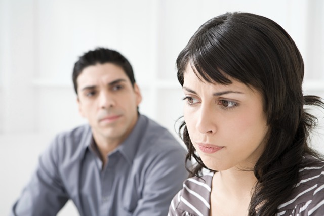 A pensive woman with her husband out of focus behind her