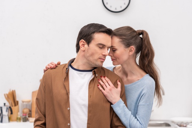 A couple embracing at home in front of a white brick wall