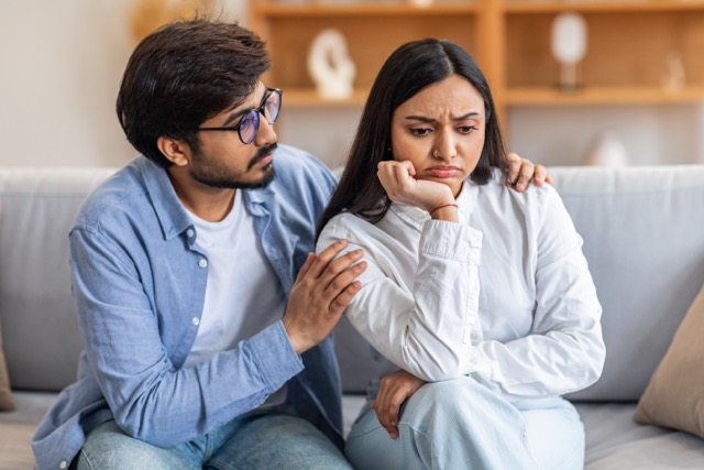 A man gently consoling an upset woman beside him on the couch