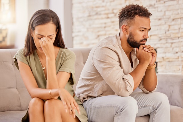A married couple sitting on the sofa, both lost in thought