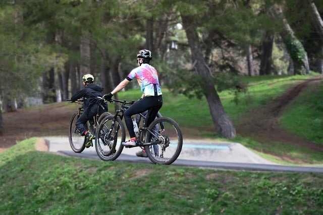 Two cyclists riding together through a green park