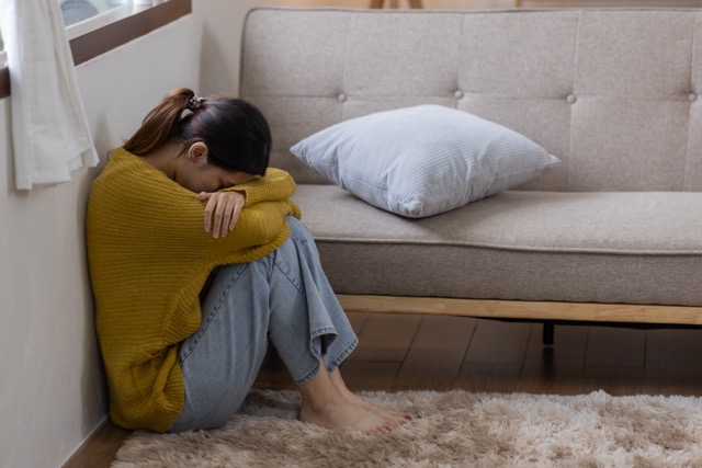 A woman sitting alone on the floor at home, crying