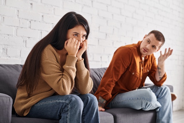 A discouraged man talking to his offended wife on the living room couch