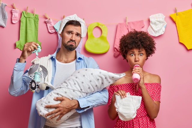 New parents looking exhausted, one holding the baby and the other a bottle