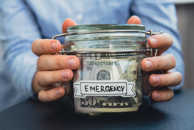 Hands putting money into a glass jar, building an emergency fund