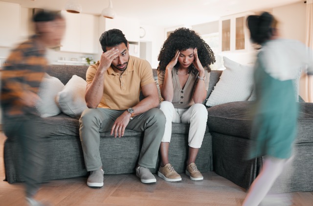 Frustrated parents holding their heads while their children play around them