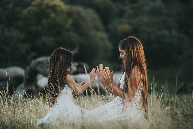 Two girls sitting in a grassy field playing a hand clapping game