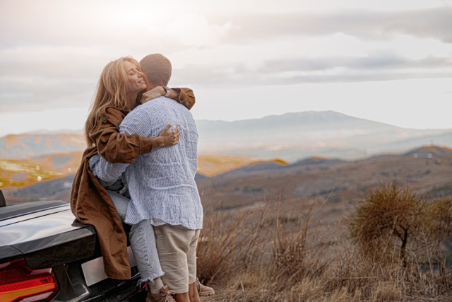 A woman hugging her husband while sitting on the back of a convertible