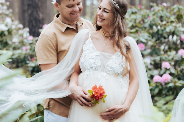 A pregnant couple hugging in a garden in blossom