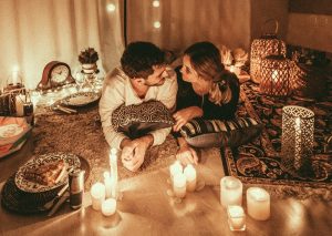 A couple lying among pillows and candles, smiling at each other