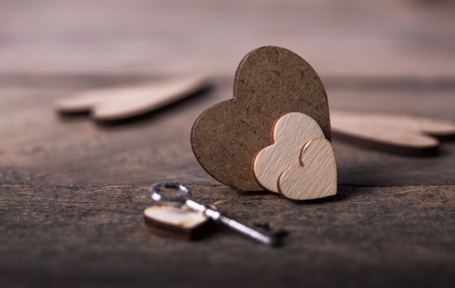 A small red heart on a dark wooden background beside a key