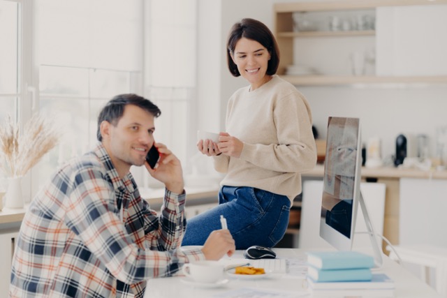 A couple in the kitchen, one on a phone call while the other stands beside him