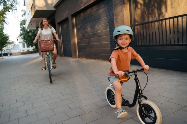 A child on a balance bike with his mother cycling behind him