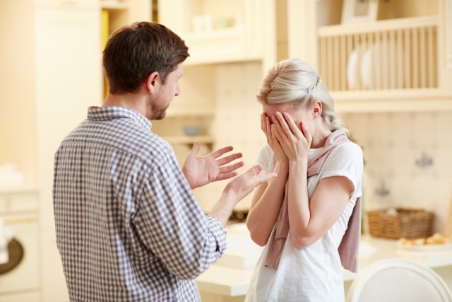 A husband talking to his upset wife, who is covering her face with her hands