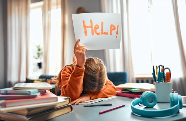 A child at a desk hiding her face while struggling with homework
