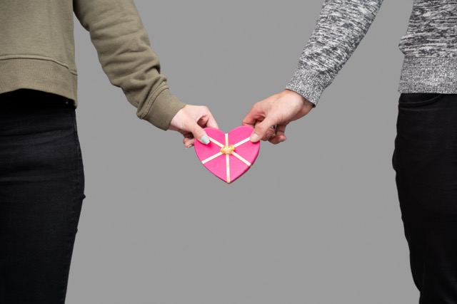 Two pairs of hands holding a pink heart shaped box