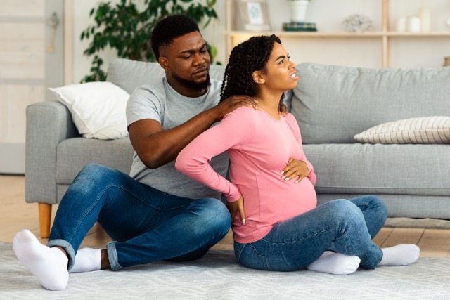 A pregnant woman with back pain, sitting on the living room floor