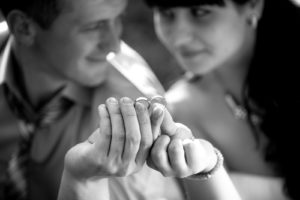A smiling couple holding their wedding rings