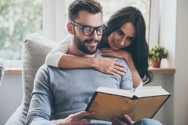 A woman leaning against her husband while he reads on the couch