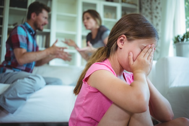 A sad girl listening to her parents arguing at home