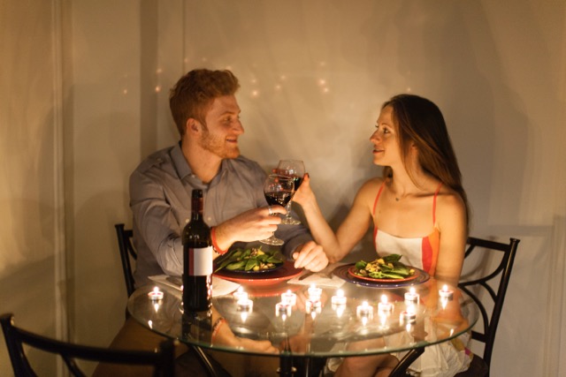 A couple face to face at a candlelit meal, making a toast