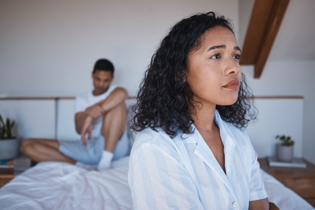 An unhappy couple sitting apart on the bed