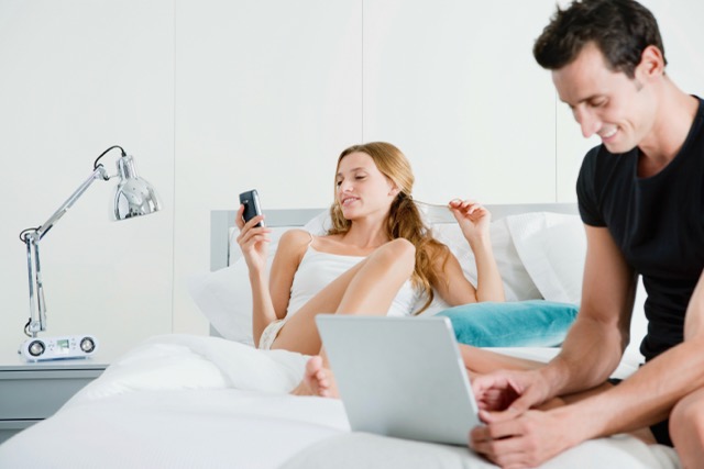 A couple on the bed, each on their own screen