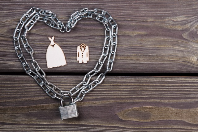 Miniature wedding clothes framed by heart shaped chains and a padlock