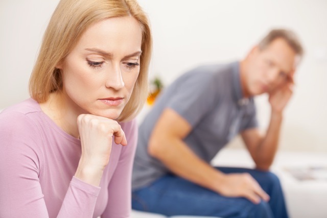 A woman in the foreground and a sad man behind her