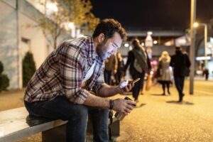 A man sitting on a bench, smiling at his phone