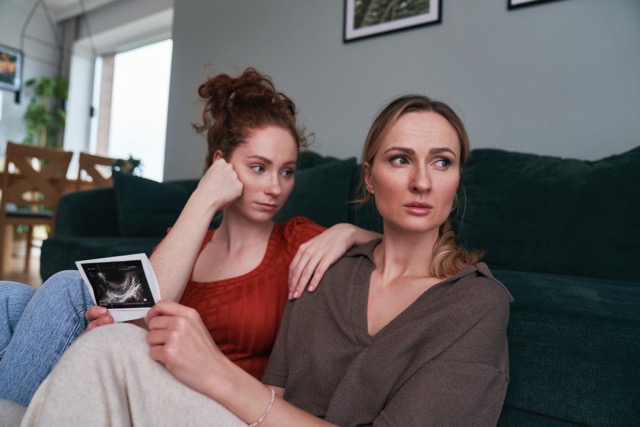 A woman holding an ultrasound scan while a friend consoles her
