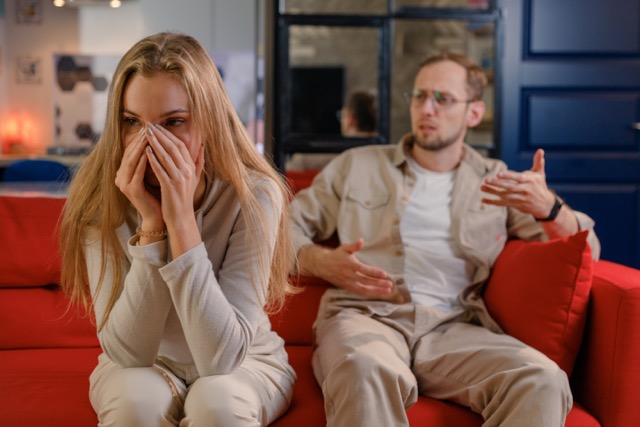 A young couple in a relationship crisis, sitting separately on the sofa after a quarrel