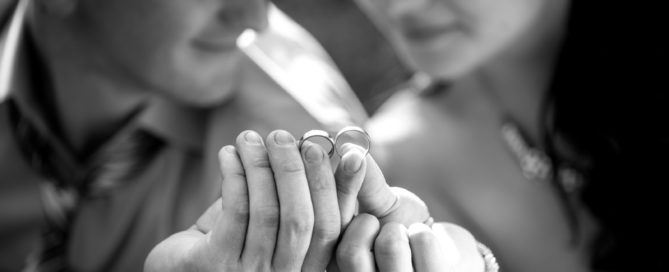 Smiling couple holding wedding rings next to each other