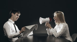 Angry wife shouting into a megaphone while oblivious husband reads newspaper
