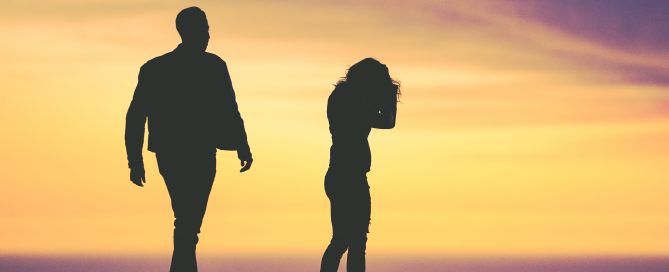 Silhouetted couple walking apart from each other on the beach at sunset