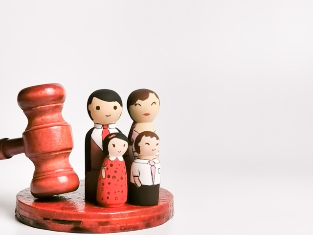 The image features a wooden gavel with a set of painted wooden family figurines, symbolizing a family unit.