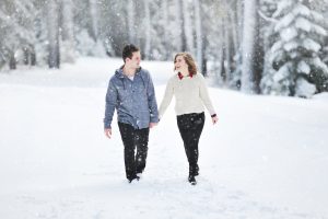 Young couple holding hands and smiling walking in snowy forest