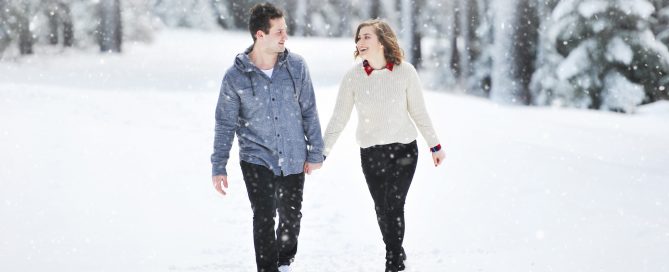 Young couple holding hands and smiling walking in snowy forest