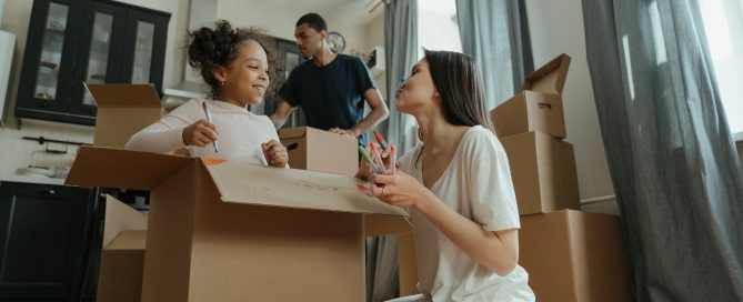 Young couple and child unpacking in a kitchen filled with cardboard boxes