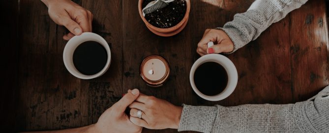 Aerial shot of two coffee cups and focus on couple holding hands