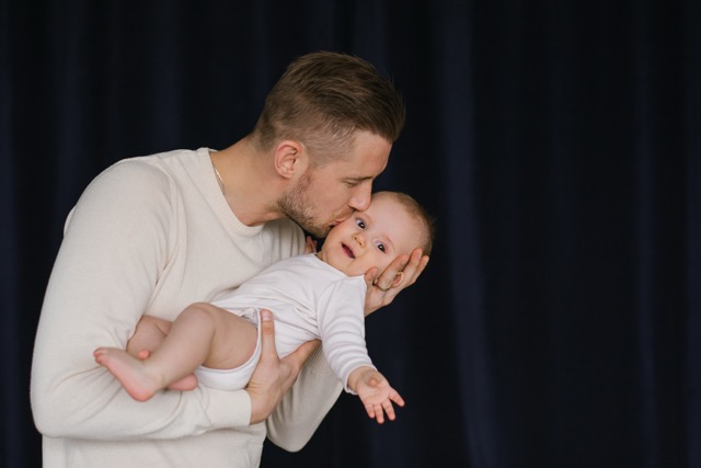 A happy father holds his baby son in his arms in the house and kisses him