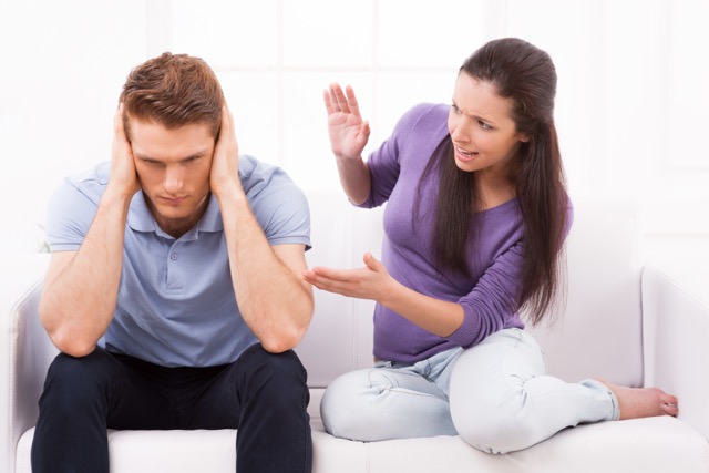 Stupid Arguments in Marriage: 
Are you with me? Furious young woman shouting and gesturing while man sitting close to her on the couch and holding head in hands