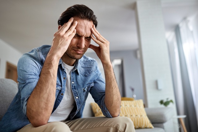 Low angle view of distraught man holding his head in pain while sitting in the living room.