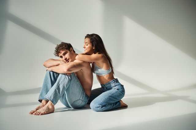 Sex-Starved Relationship:happy young woman in satin bra and jeans posing with shirtless man on grey background, closeness