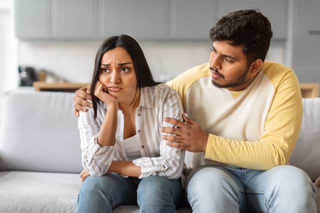 Feeling Smothered in Relationships: marriag couple comforting his distressed girlfriend while sitting together on sofa, caring eastern husband expressing concern and support to depressed wife while they relaxing at home, closeup