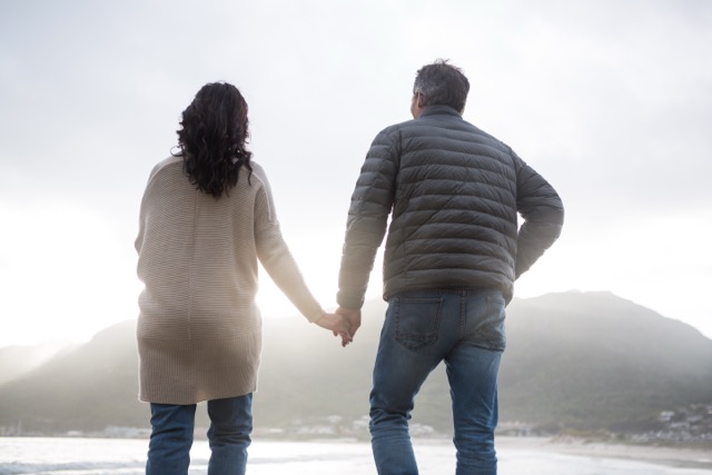 Rear view of couple holding hands on beach during winter