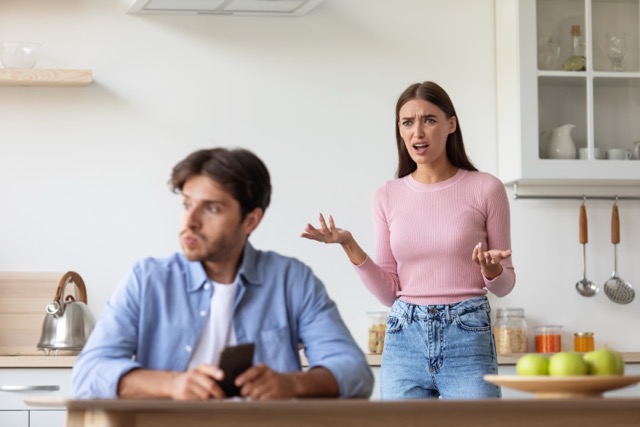 Sad angry upset offended young wife yelling at husband with smartphone on kitchen interior. Negative emotions, problems in relationships, addiction on social networks, online game, device at home