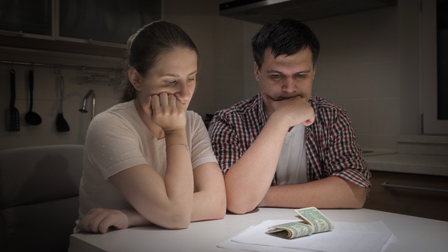 Financial Anxiety: Stressed couple sitting on kitchen at night and looking on few money banknotes left.