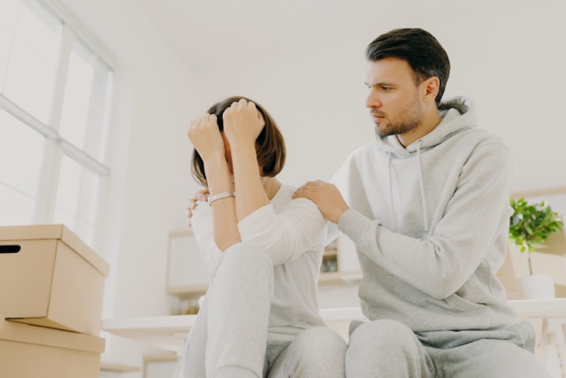 Stressful family couple forced to move home because of financial problems, woman complaining about someting, her affectionate husband tries to calm, pose indoor, carton filled containers around