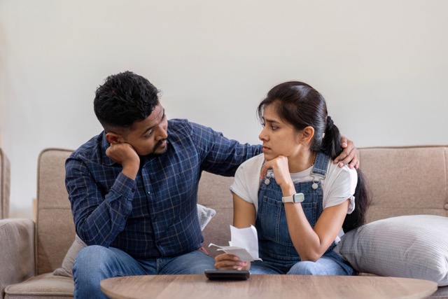 Young couple stressing about bills and invoices in living room Increased expenses cause stress.